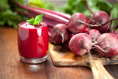 Glass of fresh beetroot juice with bets on wooden table