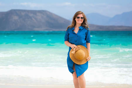 Happy traveler woman in blue dress enjoys her tropical beach vacationの写真素材