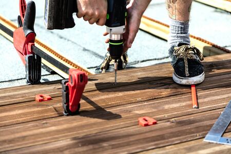 Handyman installing wooden flooring in patio, working with drilling machine.の写真素材
