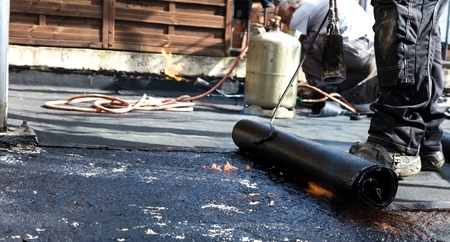 Flat roof installation. Heating and melting bitumen roofing felt.