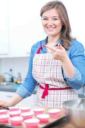 Pretty young woman baking tasty muffins at home.の写真素材