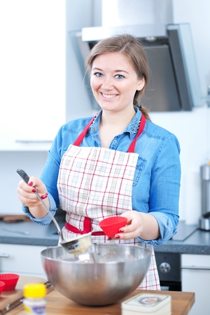 Pretty young woman baking tasty muffins at home.の写真素材