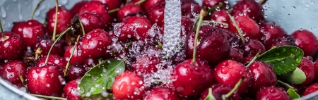 Washing sweet cherries in metal colander under water jet close-up..