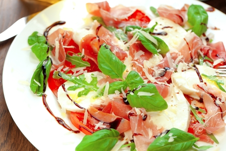 Plate of healthy classic delicious caprese salad with ripe tomatoes and mozzarella cheese with fresh basil leaves on white wooden backgroundの写真素材