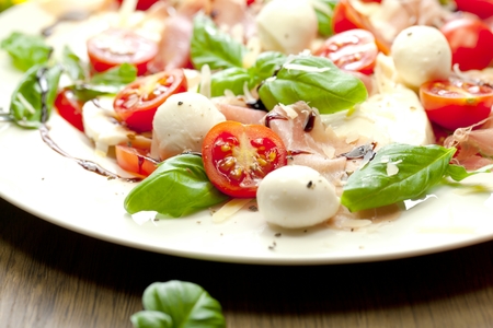 Plate of healthy classic delicious caprese salad with ripe tomatoes and mozzarella cheese with fresh basil leaves on white wooden backgroundの写真素材