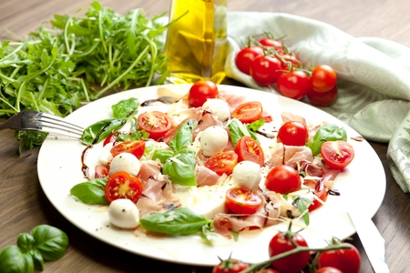 Plate of healthy classic delicious caprese salad with ripe tomatoes and mozzarella cheese with fresh basil leaves on white wooden backgroundの写真素材