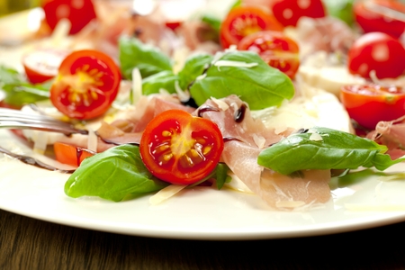 Plate of healthy classic delicious caprese salad with ripe tomatoes and mozzarella cheese with fresh basil leaves on white wooden backgroundの写真素材