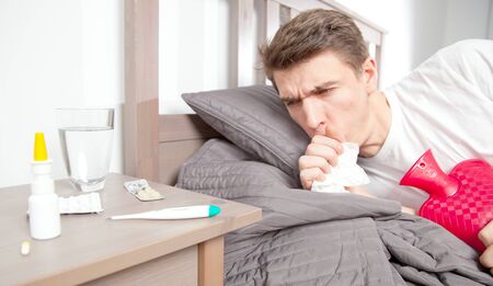 Man feeling bad lying in the bed and coughingの写真素材