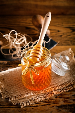 Honey with wooden honey dipper on wooden tableの写真素材