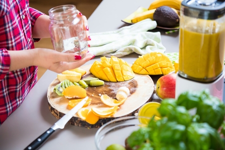 Young smiling woman making smoothie with fresh greens in the blender in kitchen at home.の写真素材