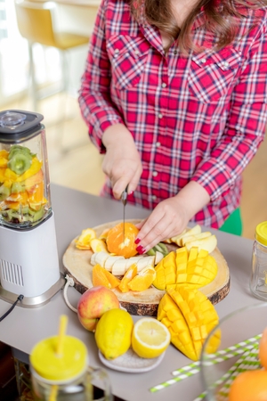 Young smiling woman making smoothie with fresh greens in the blender in kitchen at home.の写真素材