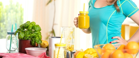 Fitness young woman drinking orange smoothie in Kitchen