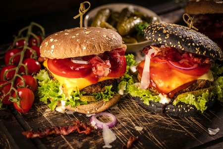 Black burger with meat patty, cheese, tomatoes, mayonnaise. Dark wooden rustic table. Modern fast food lunch.の写真素材