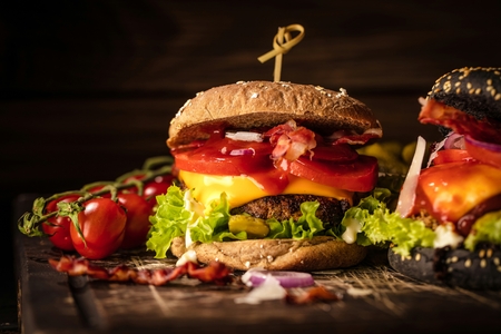 Black burger with meat patty, cheese, tomatoes, mayonnaise. Dark wooden rustic table. Modern fast food lunch.の写真素材
