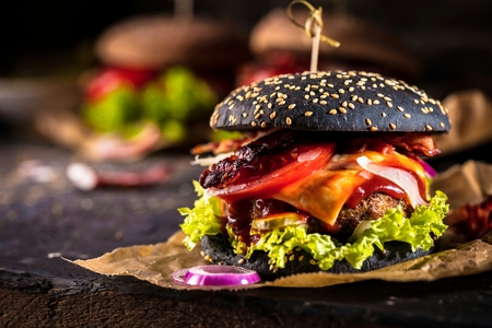 Black burger with meat patty, cheese, tomatoes, mayonnaise. Dark wooden rustic table. Modern fast food lunch.の写真素材