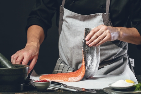 The big salmon is in the hands of the chef cook. He is using a knife to slice salmon fillet.の写真素材