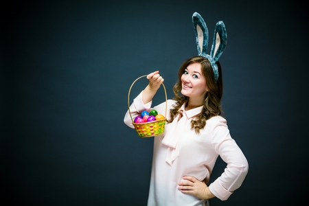 Studio shot of a happy young woman wearing bunny ears and holding up a colorful Easter egg
