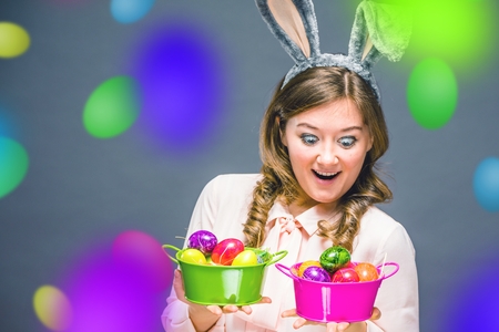 Studio shot of a happy young woman wearing bunny ears and holding up a colorful Easter egg in front of her eyeの写真素材