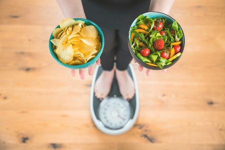 Healthy young woman looking at healthy and unhealthy  food, trying to make the right choiceの写真素材