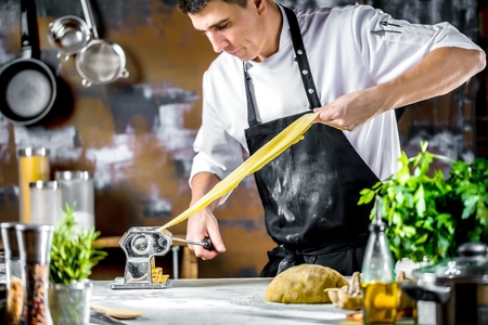 Chef making spaghetti noodles with pasta machine on kitchen table with some ingredients around.の写真素材