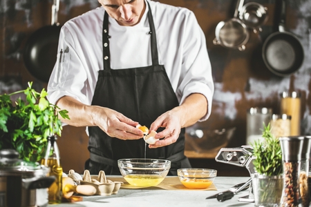 Closeup photo of baker cracking egg for dough.の写真素材