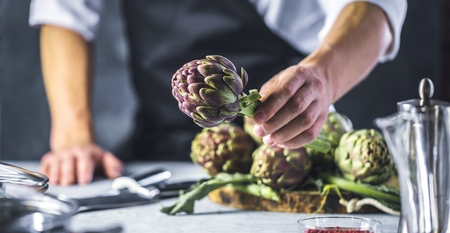 Chef cutting artichokes for dinner preparation - Man cooking inside restaurant kitchenの写真素材