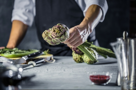 Chef cutting artichokes for dinner preparation - Man cooking inside restaurant kitchenの写真素材