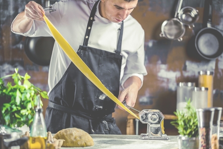 Chef making spaghetti noodles with pasta machine on kitchen table with some ingredients around.の写真素材