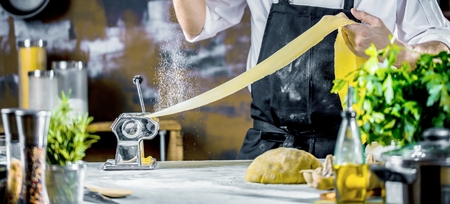 Chef making spaghetti noodles with pasta machine on kitchen table with some ingredients around.の写真素材