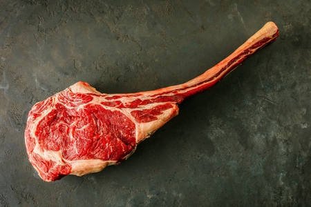 Dry aged raw tomahawk beef steak with ingredients for grillingの写真素材