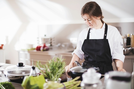 Smiling female chef in uniform is standing in the kitchen at the restaurant.の写真素材