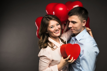 Young couple with heart shaped red balloons near grey wall.の写真素材