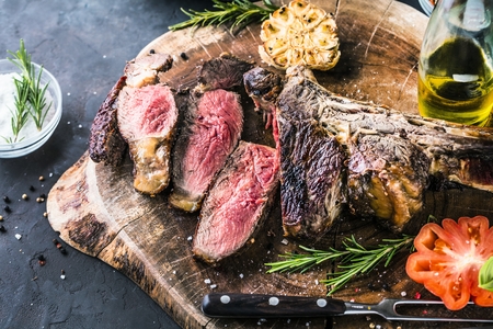 Sliced rare grilled or barbecued tomahawk beef steak on a griddle with fresh rosemary and tomato in a close up viewの写真素材
