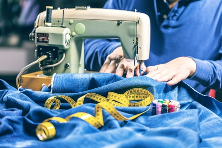 Sewing denim jeans with sewing machine. Repair jeans by sewing machine. Alteration jeans, hemming a pair of jeans, handmade garment industrial conceptの写真素材