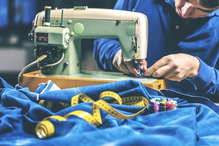 Sewing denim jeans with sewing machine. Repair jeans by sewing machine. Alteration jeans, hemming a pair of jeans, handmade garment industrial conceptの写真素材