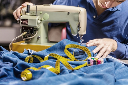 Sewing denim jeans with sewing machine. Repair jeans by sewing machine. Alteration jeans, hemming a pair of jeans, handmade garment industrial conceptの写真素材
