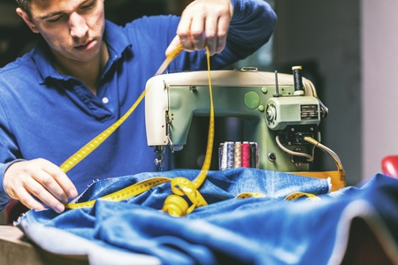 Sewing denim jeans with sewing machine. Repair jeans by sewing machine. Alteration jeans, hemming a pair of jeans, handmade garment industrial conceptの写真素材