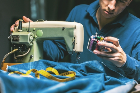Sewing denim jeans with sewing machine. Repair jeans by sewing machine. Alteration jeans, hemming a pair of jeans, handmade garment industrial conceptの写真素材