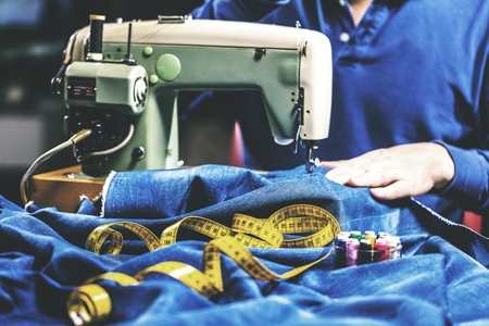 Sewing denim jeans with sewing machine. Repair jeans by sewing machine. Alteration jeans, hemming a pair of jeans, handmade garment industrial conceptの写真素材