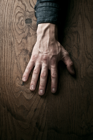 A hand, placed on the wooden background with fingers extended, symbolizing the connection between humans and nature.の写真素材