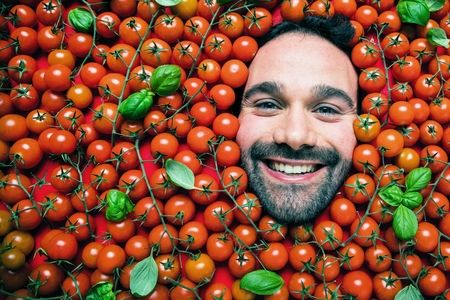 Man with tomatoes, concept for food industry. Face of emotional man in tomato surfaceの写真素材