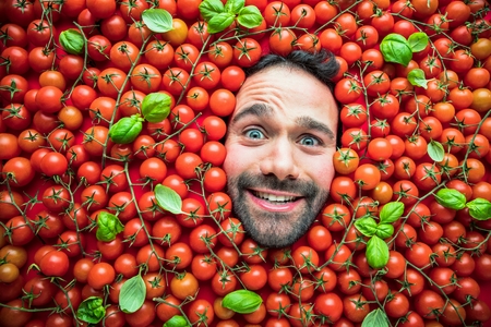 Man with tomatoes, concept for food industry. Face of emotional man in tomato surfaceの写真素材