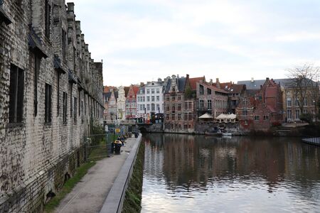 Canal in Ghent, Belgium next to a church with garbage cans on the sidewalk and historic buidlings on the other side of the water.のeditorial素材