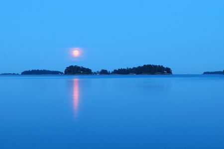 Red sun in a blue sky and reflection in the blue water in a lake in Helsinki,&#xA;Finland in the middle of the night.の写真素材