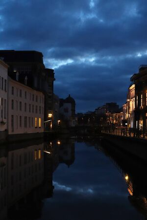 Reflections of the lit up buildings and blue sky in the water along a canal in Ghent, Belgium at night.のeditorial素材