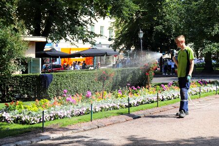 Man watering colorful flowers in a garden in Esplanadi Park in Helsinki, Finland on a hot summer day.のeditorial素材