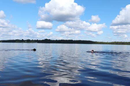 Boy and dog swimming towards each other in Lake Ranuanjarvi in Ranua, Lapland, Finland.のeditorial素材