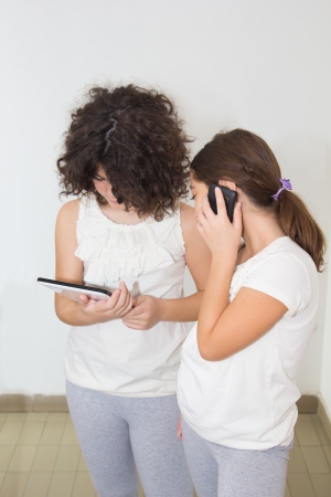 Two ten year old girls using computer tablet and smart phoneの写真素材