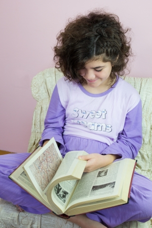 Ten year old girl in pajamas and old encyclopediaの写真素材