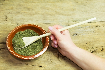 Hand holding wooden spoon of dry parsley in bowl with dry parsley, on wooden tableの写真素材